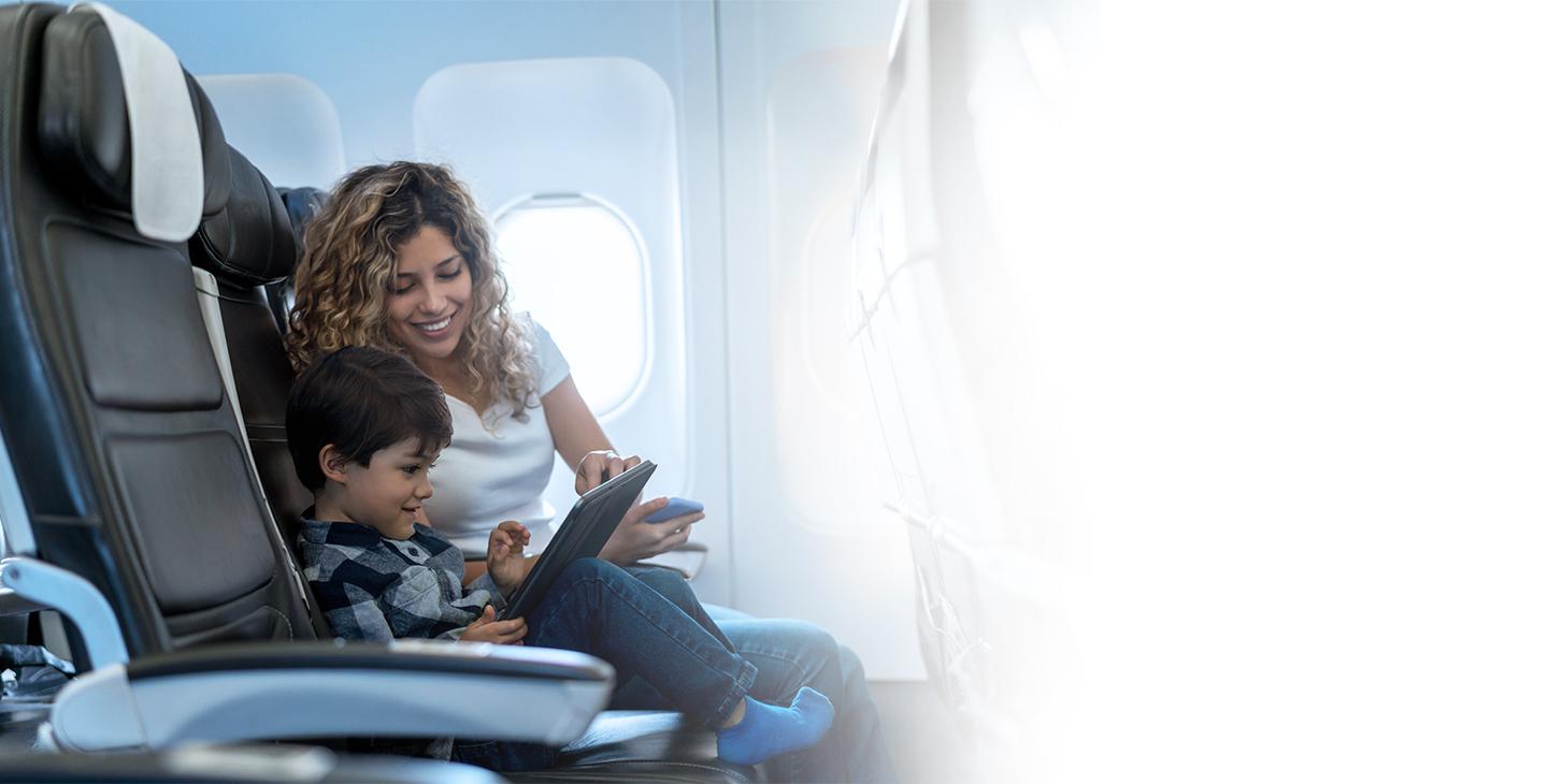 在飞机上，坐在儿子旁边的一位女士正在帮助儿子将他的平板电脑连接到飞机上的wifi
