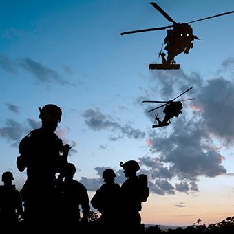 黄昏时分，五名士兵在战场上的剪影，两架直升机在上空飞行