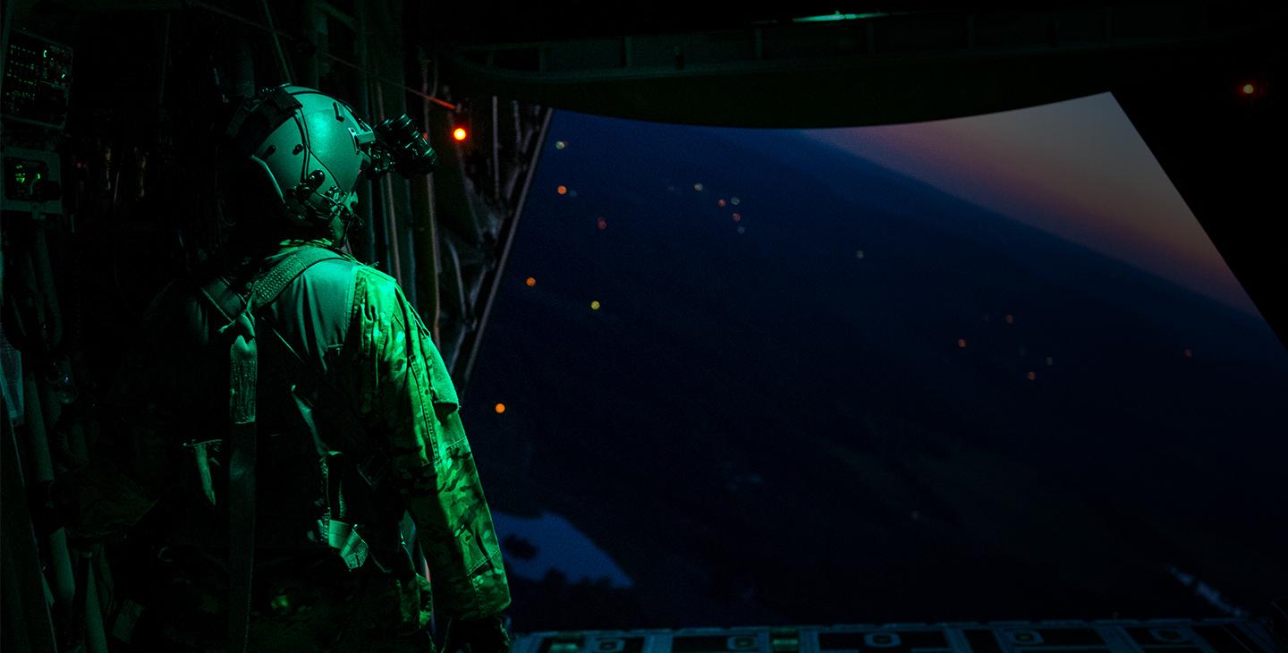 Soldier with a headset using military satcom to communicate, looking out of an aircraft at night