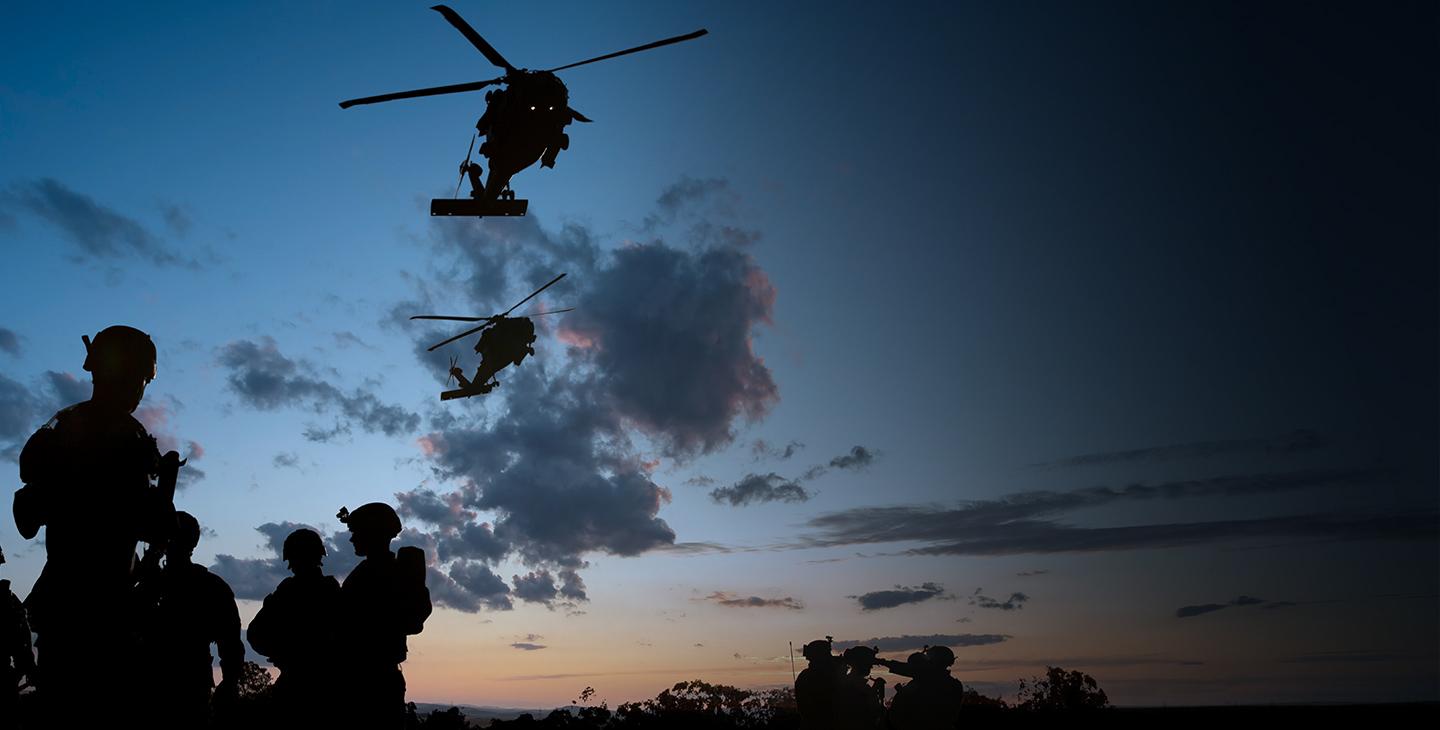 Rotary wing aircraft flying over soldiers utilizing defense technology at dusk 